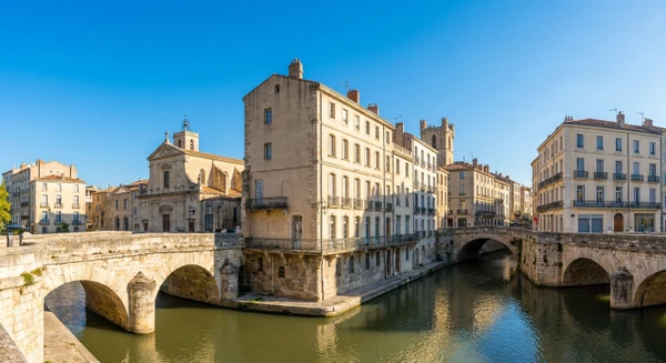 Photographie panoramique ou au niveau du sol de Narbonne, montrant l'architecture urbaine caractéristique de la ville avec ses façades de bâtiments résidentiels ou commerciaux, représentatifs du tissu urbain où intervient l'entreprise de plâtrerie et rénovation intérieure. La perspective doit clairement montrer le type de constructions (immeubles anciens ou modernes) accessibles aux services de plâtrerie, isolation et aménagement intérieur. Image sans texte, logo ou filigrane visible.